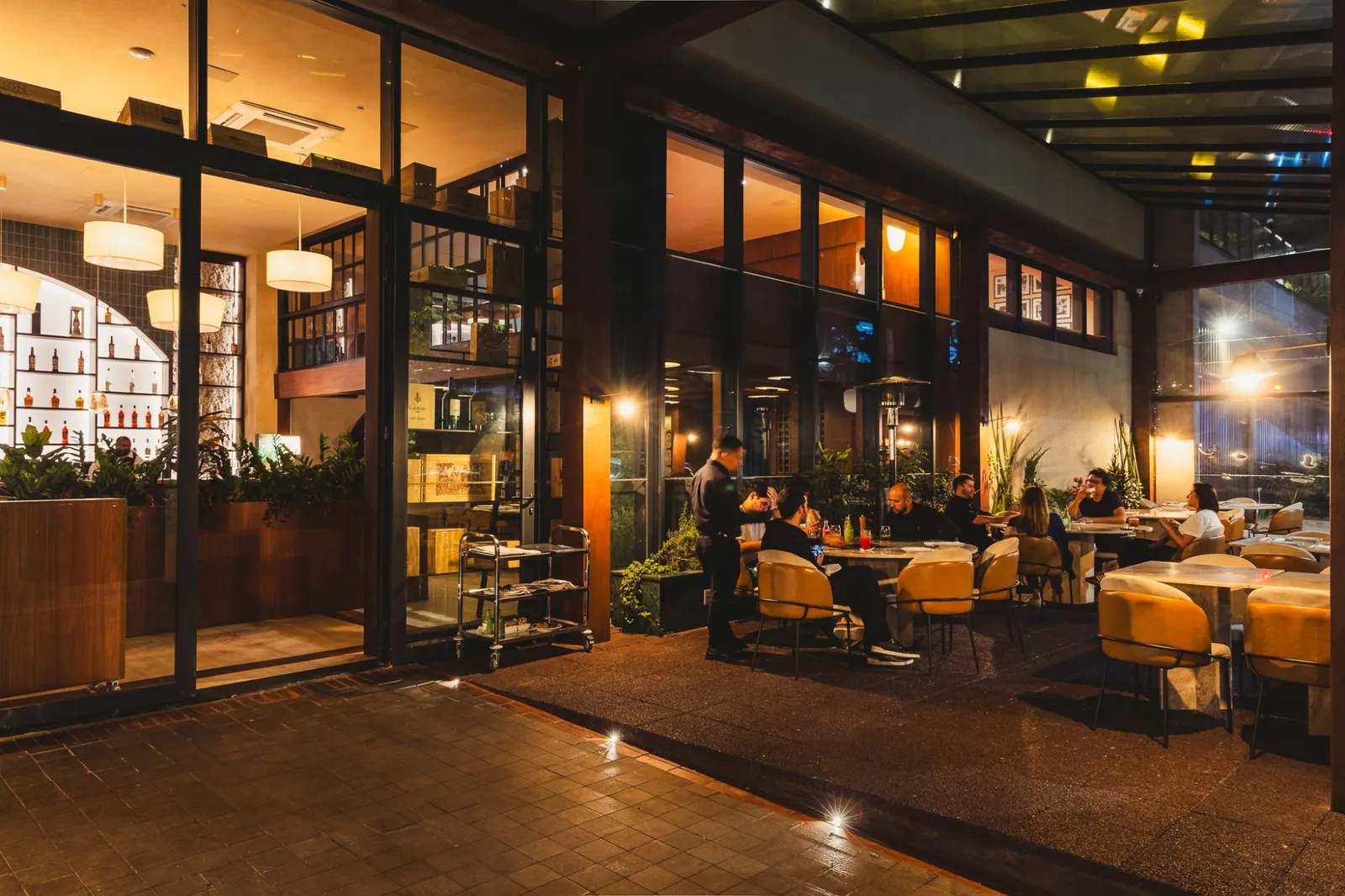 Fachada e varanda do Benvenuto Al Tavolo à noite, com clientes nas mesas